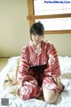 A woman in a red and white kimono sitting on a bed.