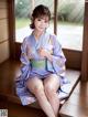 A woman in a purple kimono sitting on a wooden bench.