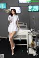 A woman in a white nurse outfit standing next to a hospital bed.