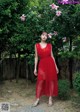 A woman in a red dress standing in front of a tree.