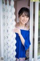 A woman in a blue top standing by a window.