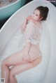 A woman in a white lingerie sitting in a bathtub.