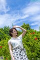 A woman standing in front of a bush with red flowers.