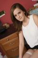 A young woman sitting on top of a bed next to a dresser.