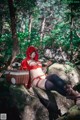 A woman in a red riding hoodie sitting on a rock in the woods.